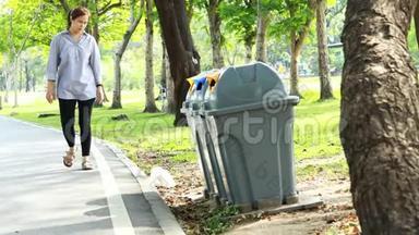 亚洲女人从地板上捡垃圾到垃圾桶，女人在公园的草地上捡垃圾塑料袋，
